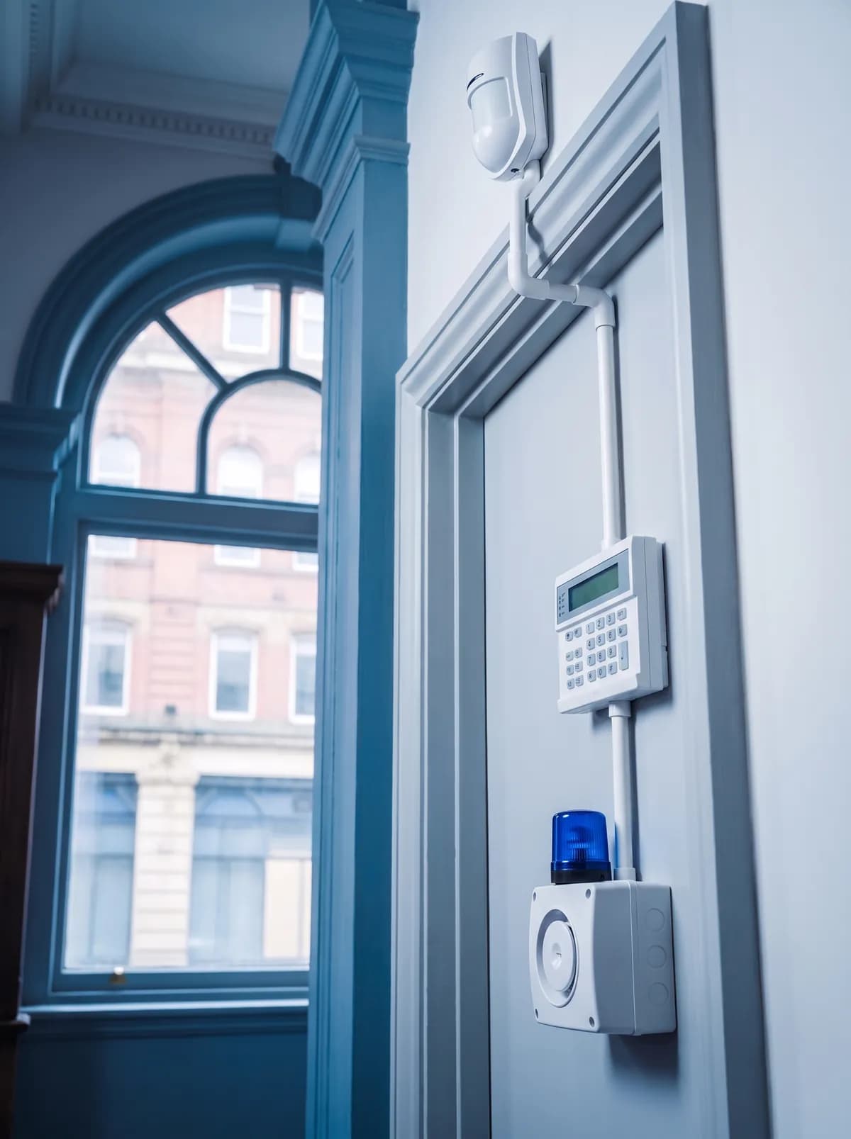 Motion detector, keypad and sounder mounted on a wall beside a window