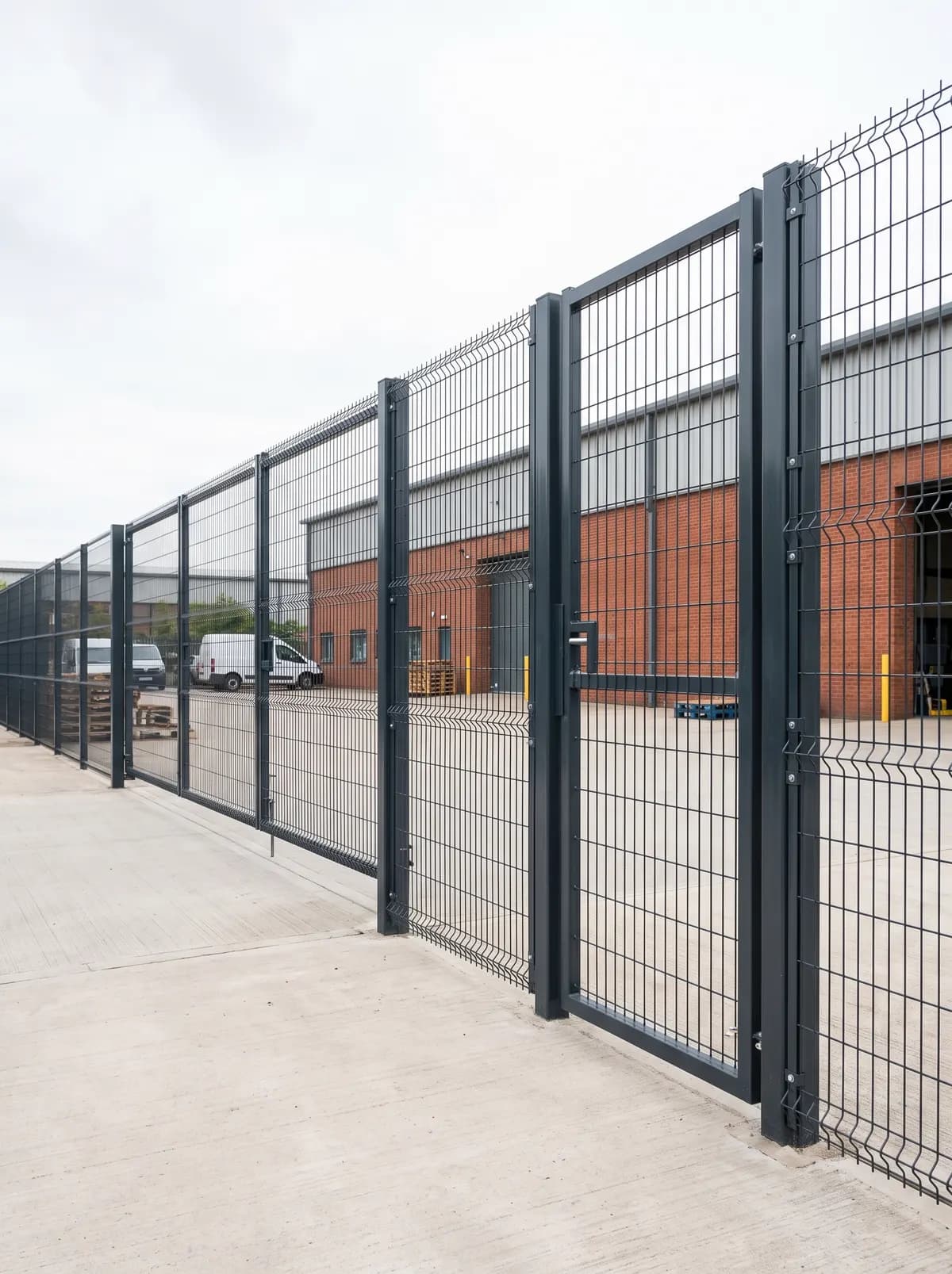 Mesh security fence and gate along a road beside an industrial building
