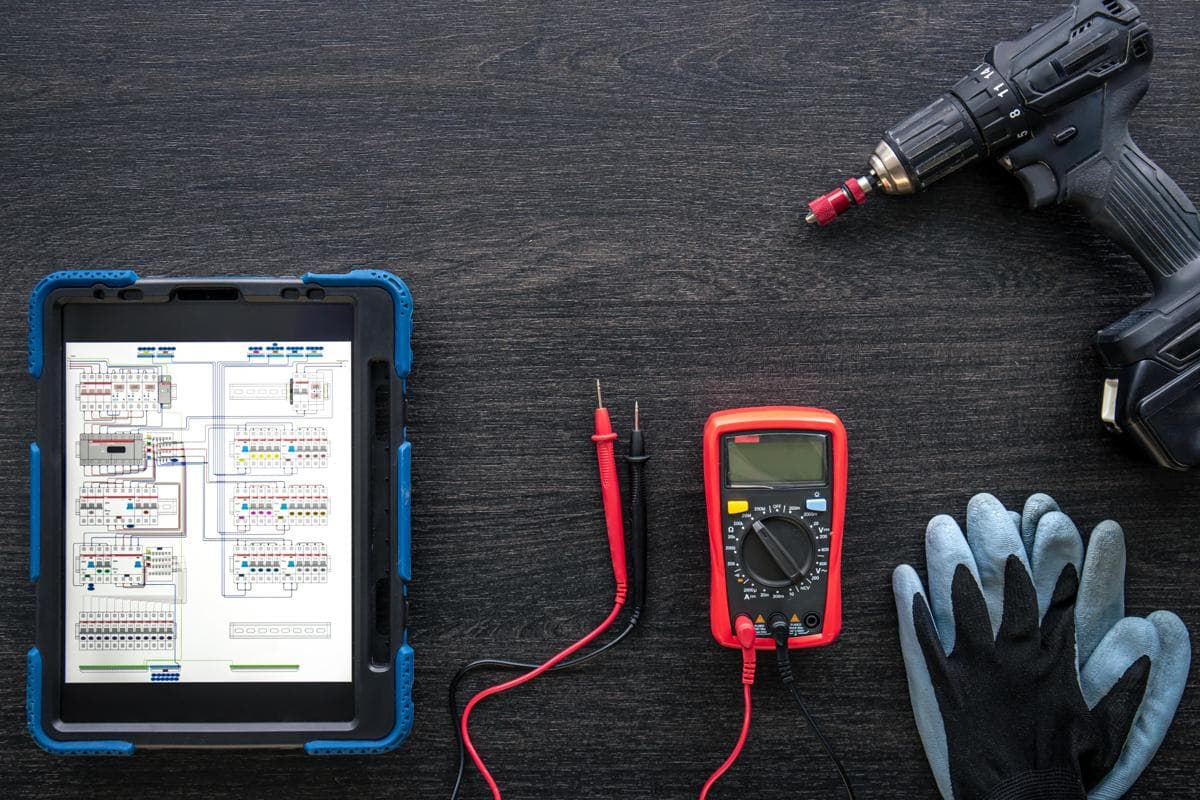 Multimeter, test leads and a tablet showing a wiring diagram on a workbench